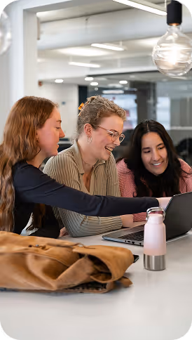 Three colleagues laughing together over a laptop in a bright office