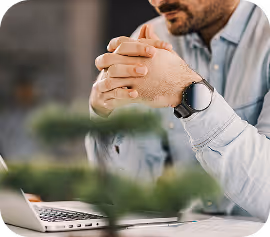 A man with clasped hands thinking in front of his laptop