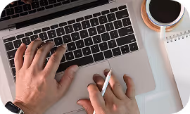 Hands typing on a laptop keyboard beside a cup of coffee